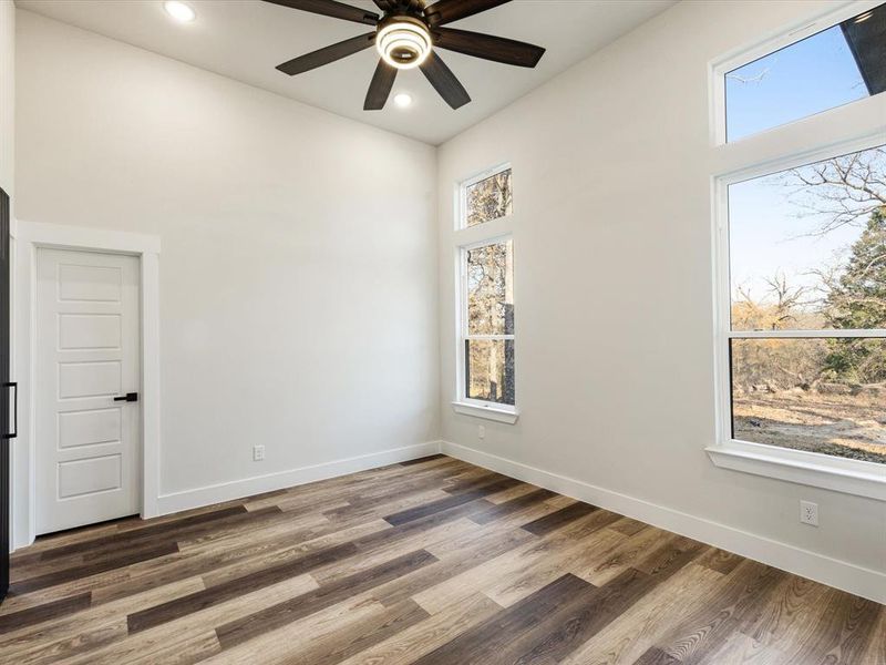 Unfurnished room featuring a high ceiling, plenty of natural light, wood finished floors, recessed lighting, and a ceiling fan Unfurnished room featuring a high ceiling, plenty of natural light, wood finished floors, recessed lighting, and a ceiling fan