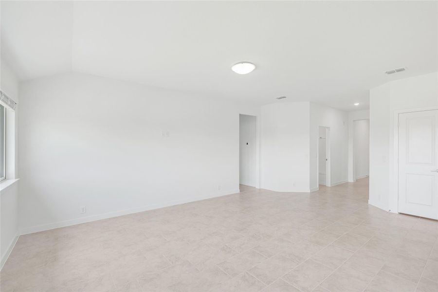 Empty room with white walls, tile floors, and a hallway leading to other rooms