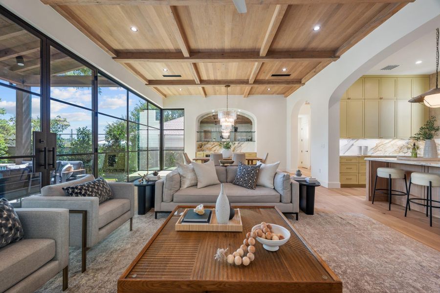 Floor-to-ceiling glass doors open this living space to the outdoors beneath a coffered wood ceiling.