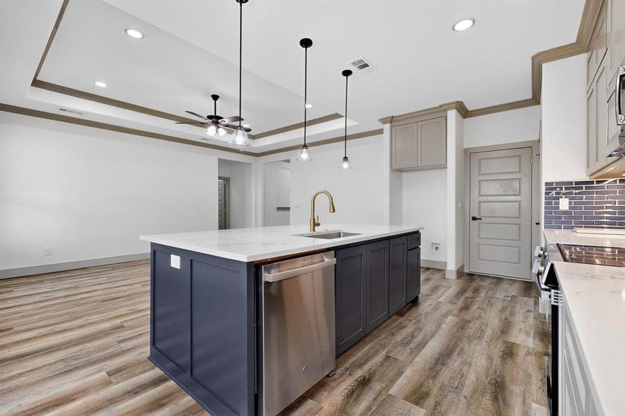 Kitchen with gray cabinets, stainless steel appliances, light stone counters, hanging light fixtures, and an island with sink