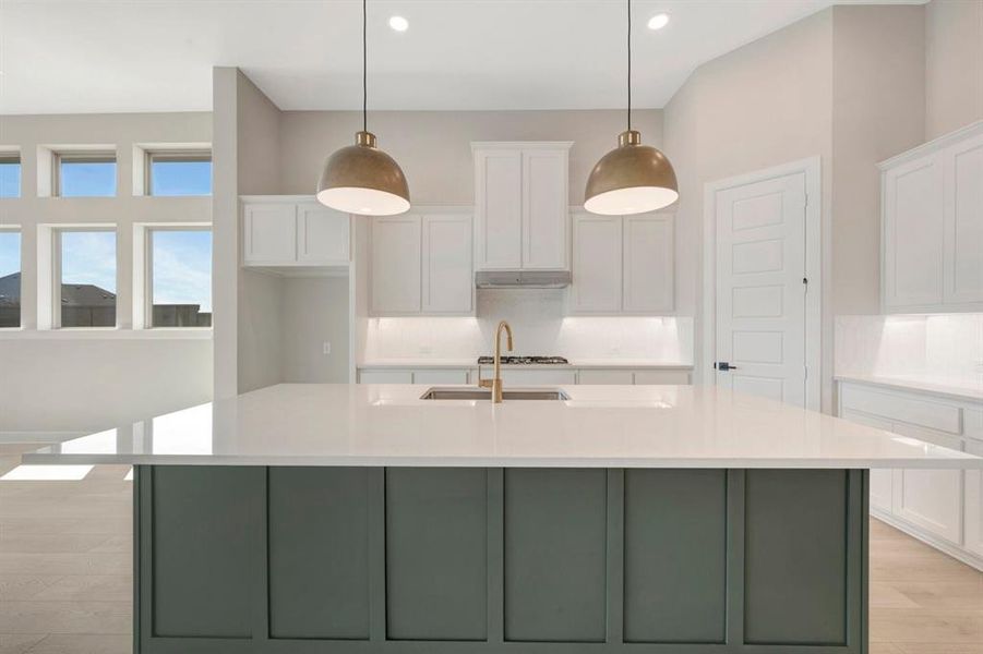 Kitchen featuring a large central island with a solid surface countertop, white shaker-style cabinetry, gold-toned pendant lighting, wood-finish flooring, and multiple windows