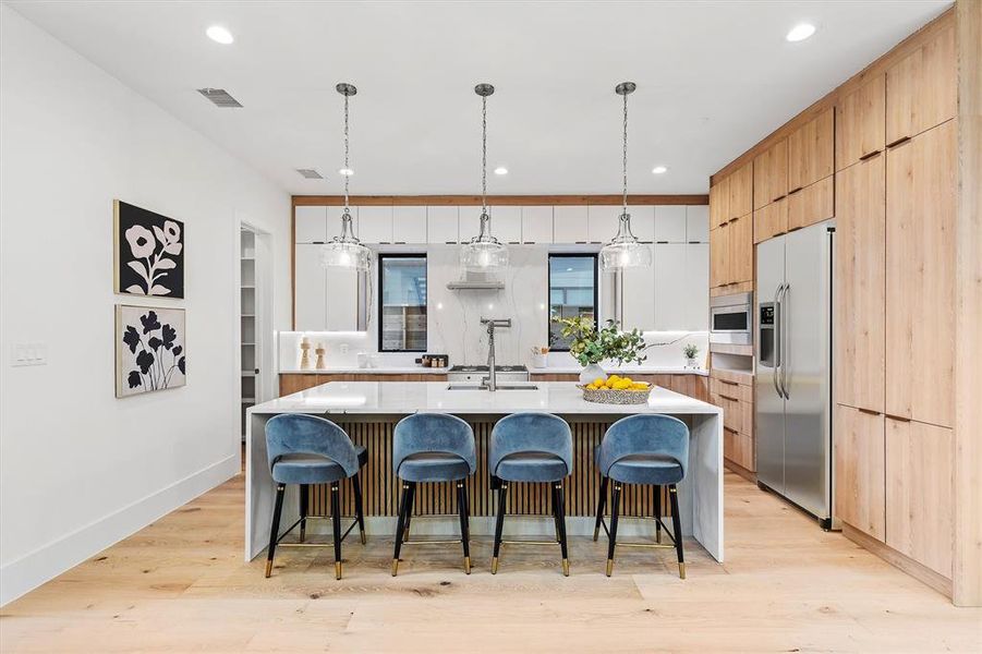 Kitchen featuring pendant lighting, a large island, appliances with stainless steel finishes, light wood-type flooring, and a kitchen bar