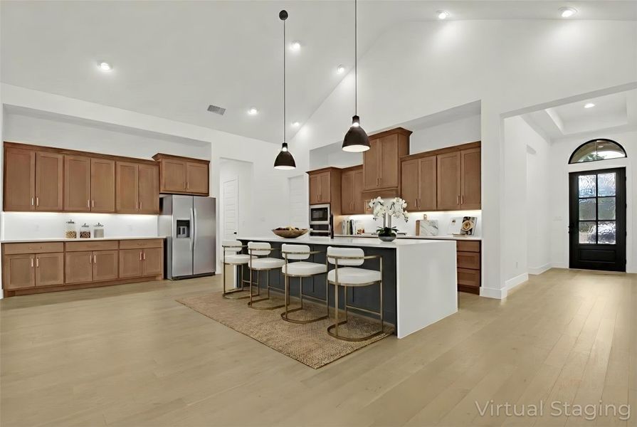 Virtually-Staged Kitchen with wood cabinetry, quartz countertops, 16ft vaulted ceiling, a kitchen breakfast bar, pendant lighting, a center island with sink, stainless steel appliances, and light hardwood floors