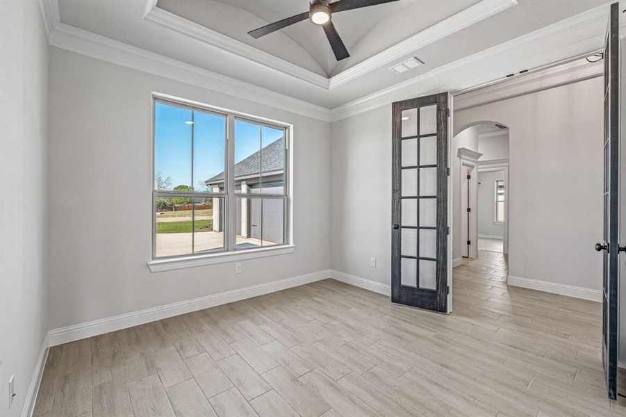 Empty room featuring a raised ceiling, arched walkways, ornamental molding, light wood-style floors, and ceiling fan