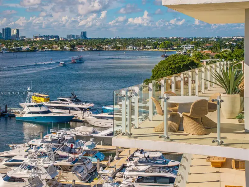Expansive private terrace featuring light-toned tile flooring and a glass panel railing overlooking a deep-water marina and coastal waterway Expansive private terrace featuring light-toned tile flooring and a glass panel railing overlooking a deep-water marina and coastal waterway