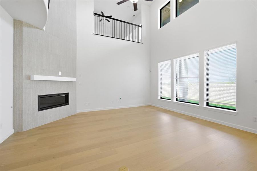 Spacious living area featuring a two-story ceiling, light wood-finish flooring, and a modern fireplace with a white mantel Spacious living area featuring a two-story ceiling, light wood-finish flooring, and a modern fireplace with a white mantel