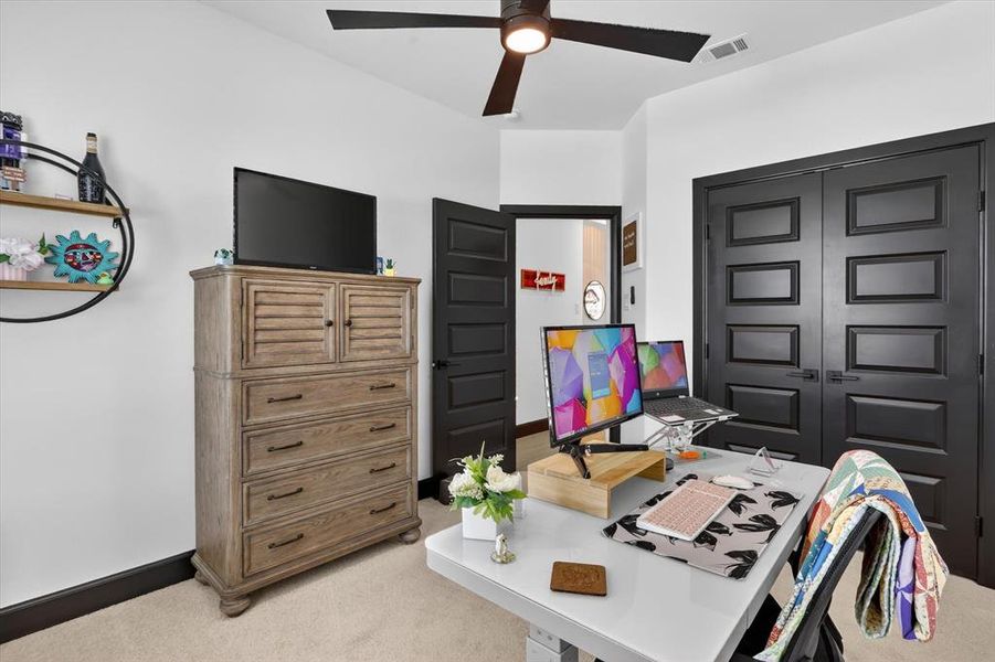 Carpeted room featuring a ceiling fan with integrated lighting, dark trim, and a white desk