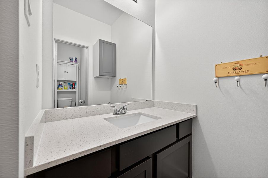 Modern bathroom with a sleek, speckled countertop and under-mount sink. Features dark cabinetry, a large mirror, and convenient storage shelves. Clean and well-lit space. Modern bathroom with a sleek, speckled countertop and under-mount sink. Features dark cabinetry, a large mirror, and convenient storage shelves. Clean and well-lit space.