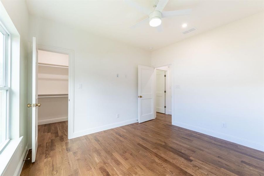 Light-filled interior featuring wood-finish flooring, a white ceiling fan with integrated lighting, and a window with white trim Light-filled interior featuring wood-finish flooring, a white ceiling fan with integrated lighting, and a window with white trim