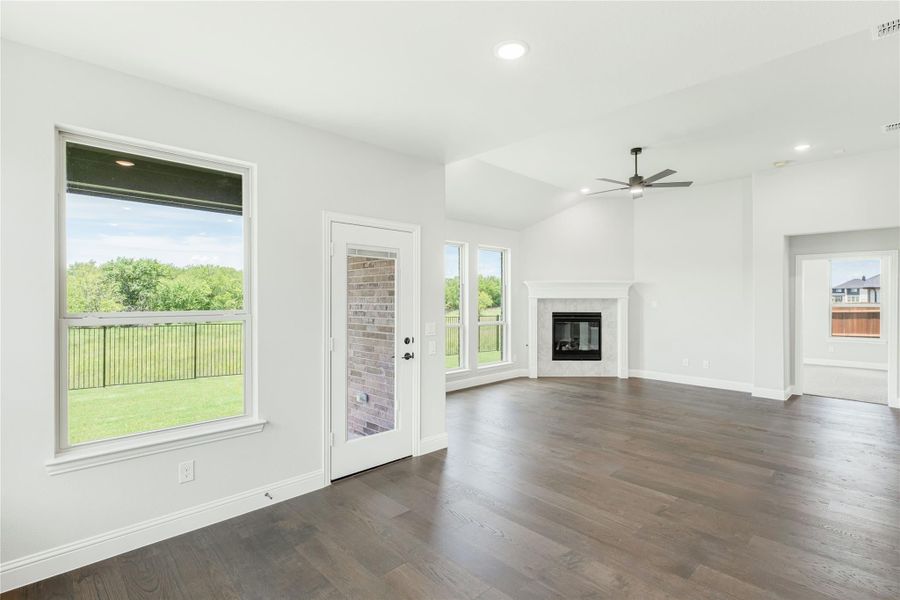 Open living room with dark hardwood floors, fireplace, ceiling fan, and large windows overlooking a backyard. Open living room with dark hardwood floors, fireplace, ceiling fan, and large windows overlooking a backyard.