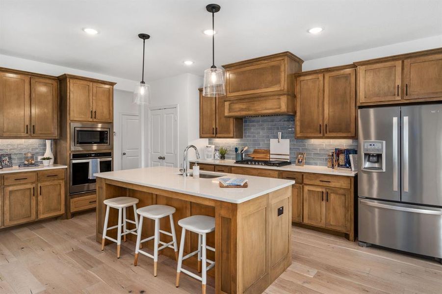 Kitchen with stainless steel appliances, sink, light wood-type flooring, and a kitchen island with sink