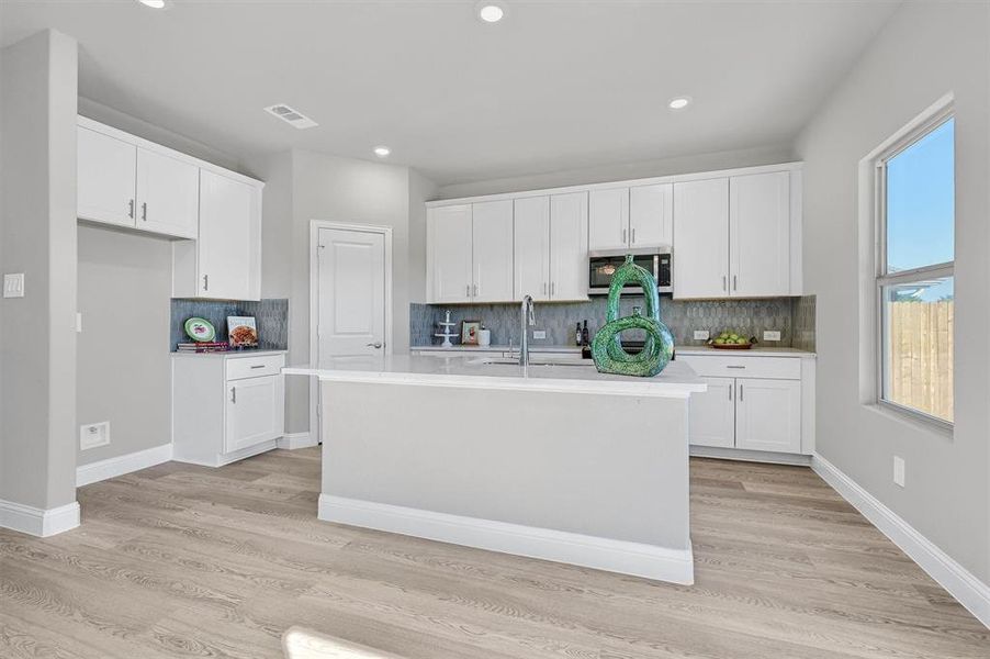 Kitchen with white cabinetry, a kitchen island with sink, plenty of natural light, and light hardwood / wood-style floors