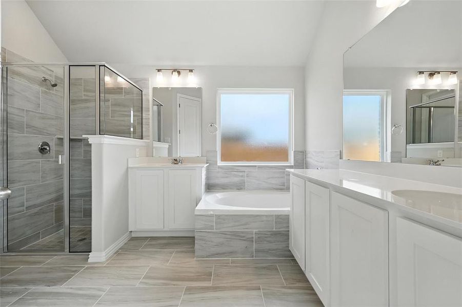 Bathroom featuring a stall shower, two vanities, a bath, and vaulted ceiling