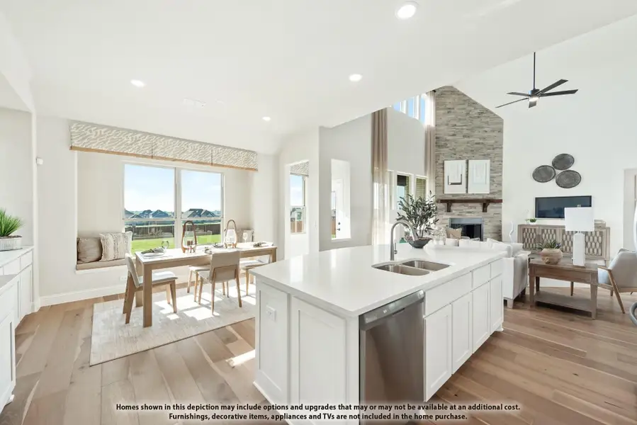 Open-concept kitchen with white island, hardwood floors, dining area, and stone fireplace in living room beyond Open-concept kitchen with white island, hardwood floors, dining area, and stone fireplace in living room beyond