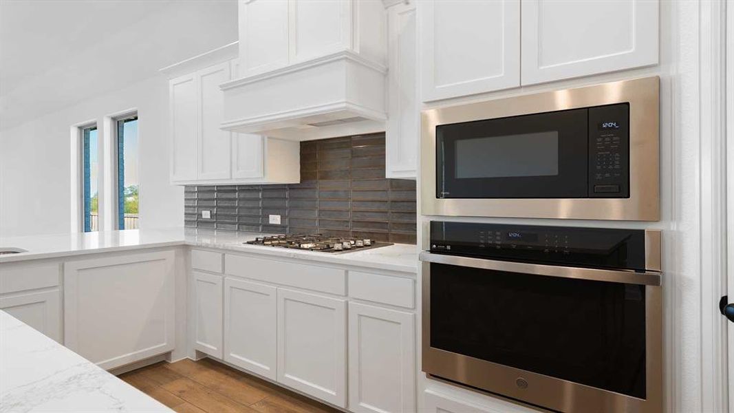 Kitchen with decorative backsplash, appliances with stainless steel finishes, light wood-type flooring, light stone counters, and white cabinets