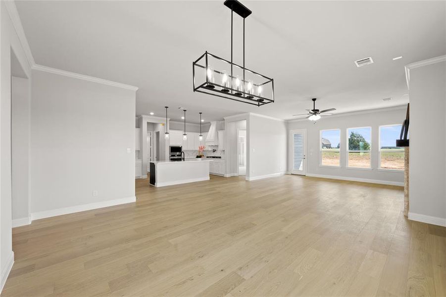 Unfurnished living room with light wood-type flooring, crown molding, and ceiling fan