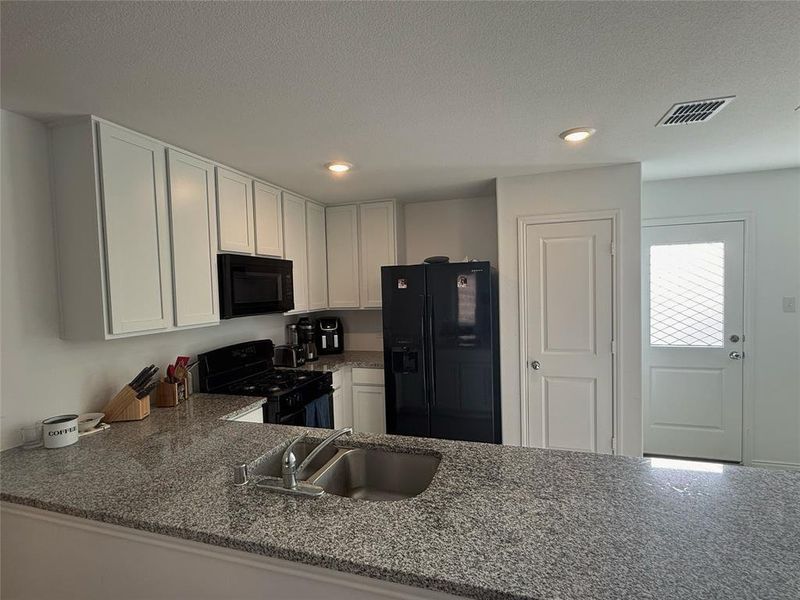 Contemporary kitchen featuring a dual basin sink, speckled stone countertops, white shaker-style cabinetry, and recessed lighting Contemporary kitchen featuring a dual basin sink, speckled stone countertops, white shaker-style cabinetry, and recessed lighting