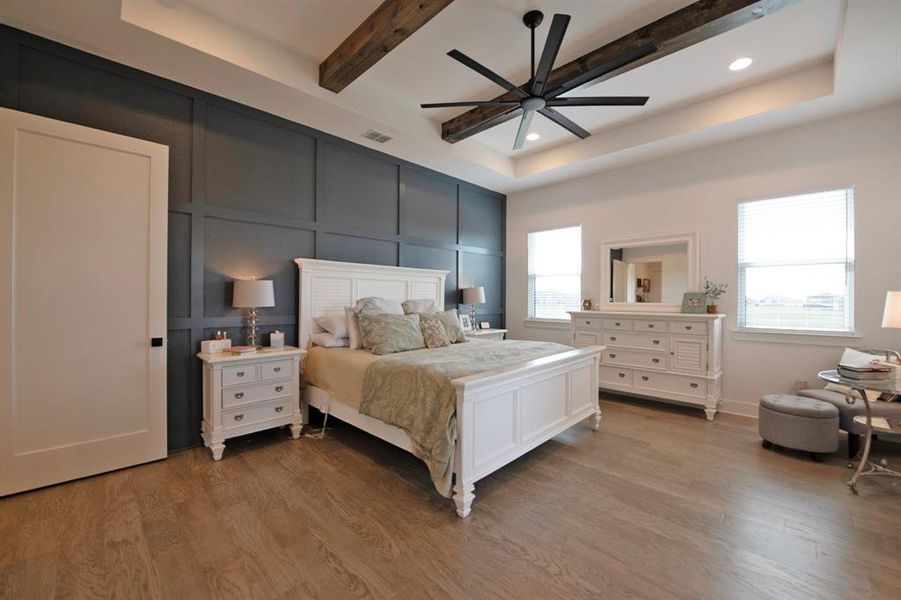 Bedroom with beamed ceiling, light wood-style floors, a decorative wall, a tray ceiling, and a ceiling fan