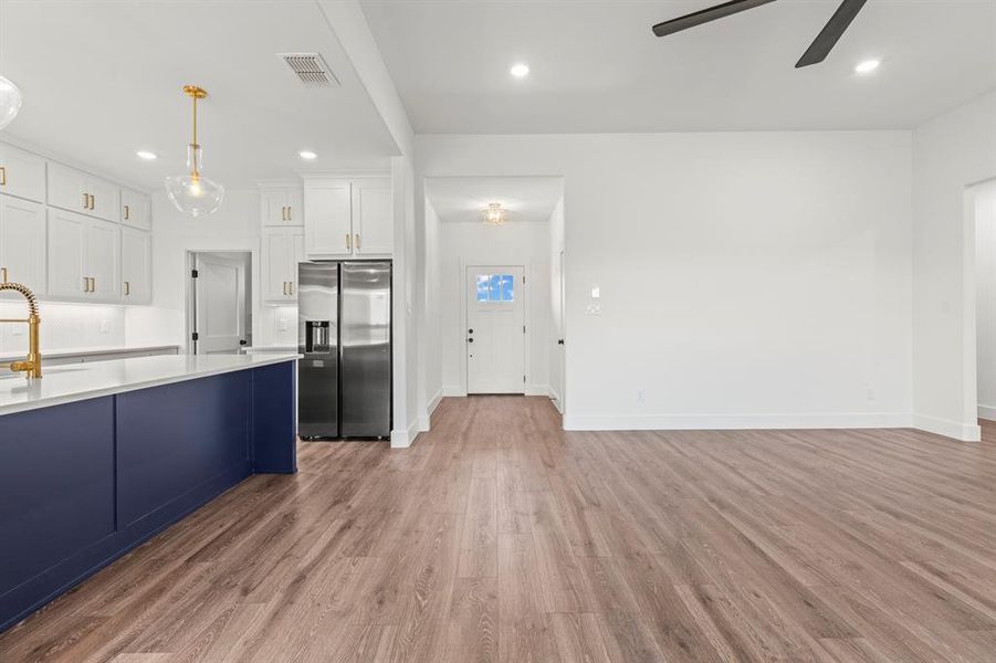 Kitchen featuring stainless steel fridge, ceiling fan, light wood-style flooring, light countertops, and white cabinetry