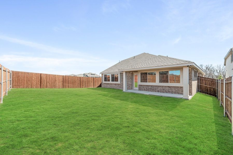 Backyard with large green lawn, brick home exterior, covered patio, and wood privacy fence Backyard with large green lawn, brick home exterior, covered patio, and wood privacy fence