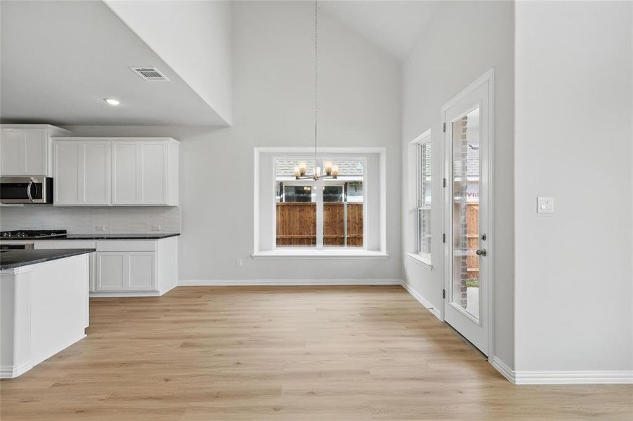 Kitchen with white cabinetry, a chandelier, light wood-style flooring, vaulted ceiling, and decorative backsplash