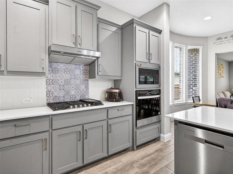Kitchen featuring grey cabinetry, white countertops, built-in stainless steel appliances, and wood-finish flooring Kitchen featuring grey cabinetry, white countertops, built-in stainless steel appliances, and wood-finish flooring
