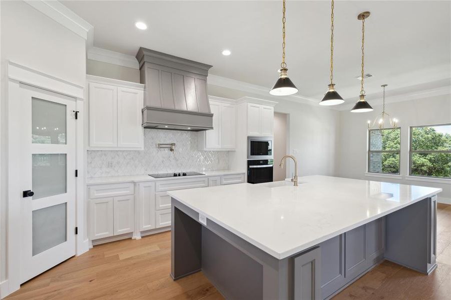 Kitchen with white cabinetry, custom range hood, a large island, black appliances, and decorative backsplash