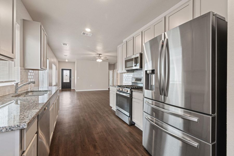 Kitchen featuring stainless steel appliances, light stone countertops, decorative backsplash, dark wood-type flooring, and recessed lighting