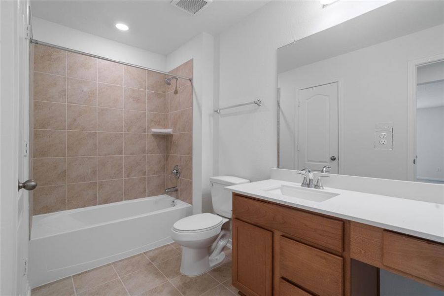 Secondary bath features tile flooring, bath/shower combo with tile surround, stained wood cabinets, beautiful light countertops, mirror, sleek fixtures and modern finishes.