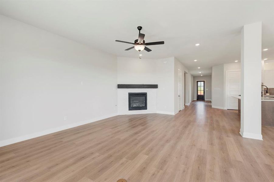 Unfurnished living room featuring a ceiling fan, a glass covered fireplace, light wood finished floors, and recessed lighting
