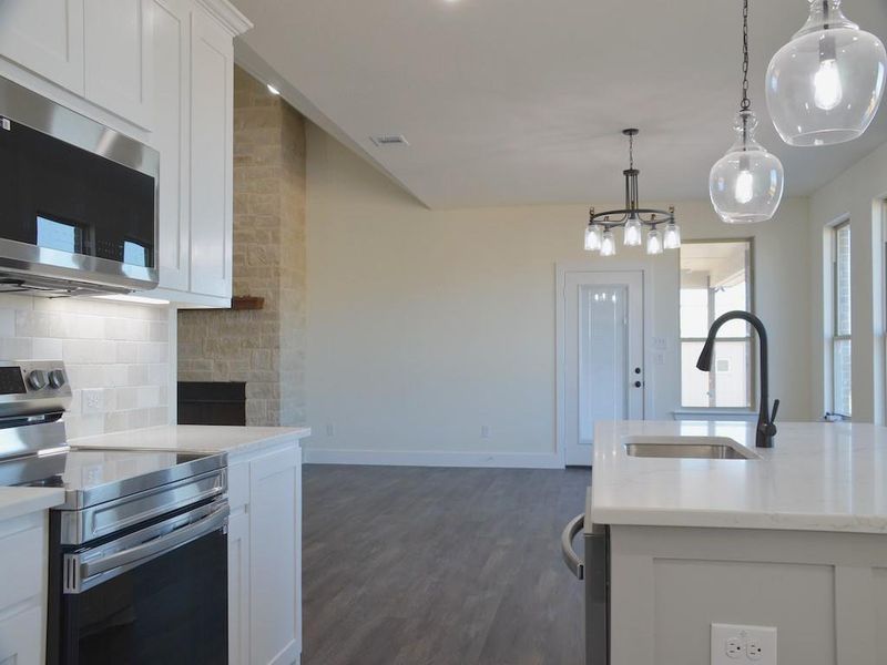 Kitchen with backsplash, stainless steel appliances, sink, decorative light fixtures, and white cabinetry