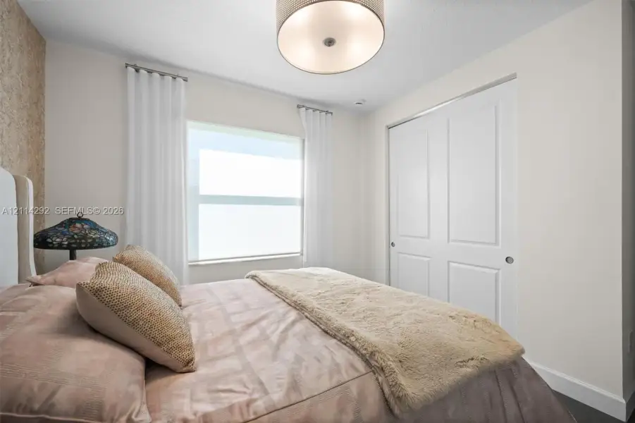 Neutral-toned interior featuring a textured accent wall, recessed lighting, a large window, and double-door closet with paneled detailing