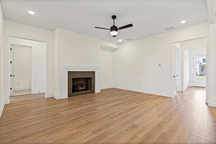 Spacious living area featuring wood-finish flooring, a fireplace with a white mantel and stone surround, and a ceiling fan with integrated lighting Spacious living area featuring wood-finish flooring, a fireplace with a white mantel and stone surround, and a ceiling fan with integrated lighting