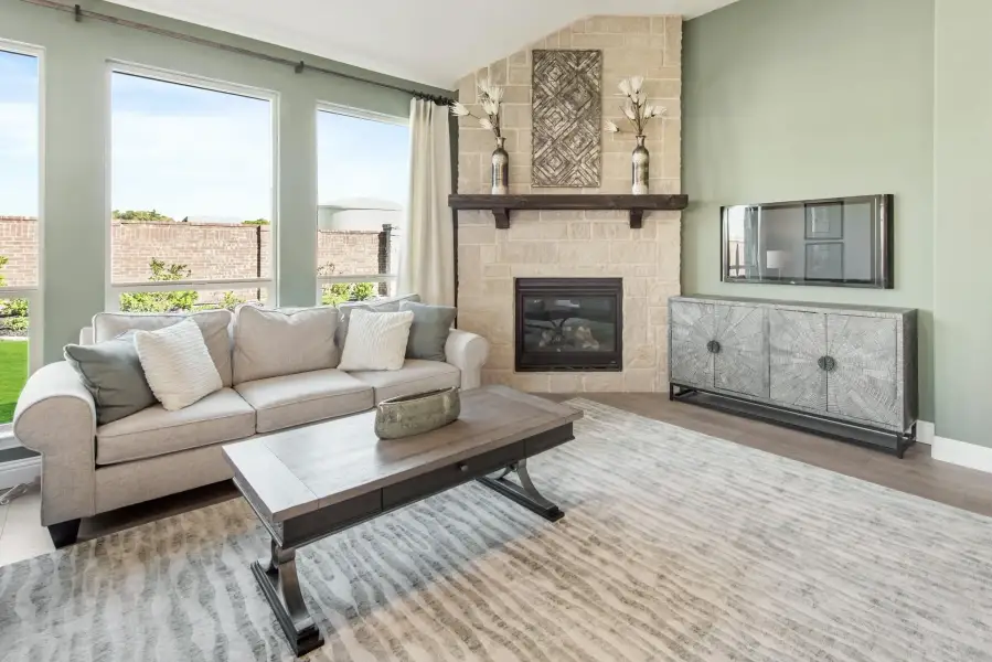 Living room with stone fireplace, neutral sofa, wood coffee table, and large windows with natural light