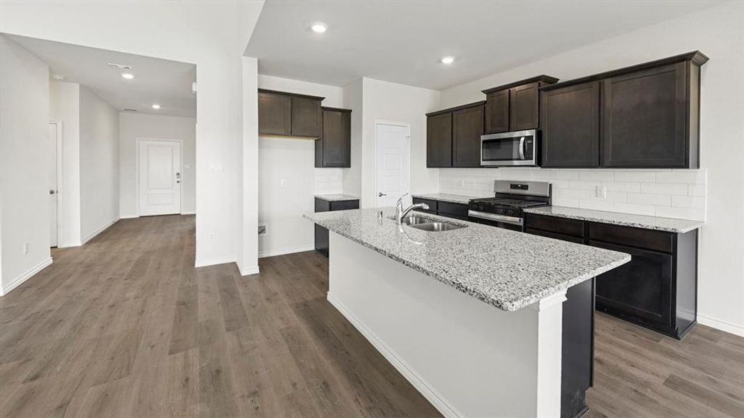Modern kitchen featuring a central island with an undermount sink, granite countertops, dark wood-finish cabinetry, stainless steel appliances, and subway tile backsplash Modern kitchen featuring a central island with an undermount sink, granite countertops, dark wood-finish cabinetry, stainless steel appliances, and subway tile backsplash