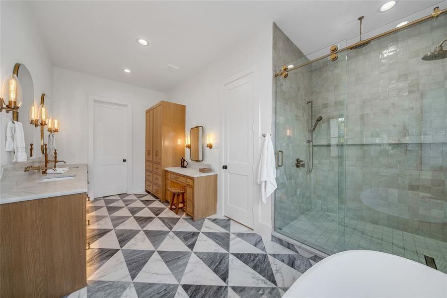 Geometric tile flooring with a dual vanity featuring brass fixtures, a glass-enclosed shower with a rainfall showerhead, and recessed lighting
