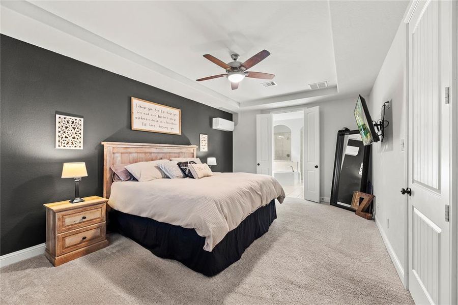 This spacious bedroom featuring a contrasting dark accent wall, plush carpeting, and ample natural light. It includes an en-suite bathroom, a ceiling fan for comfort.