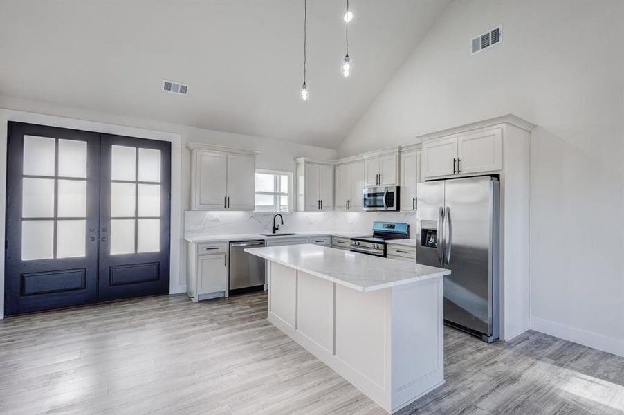 Kitchen with french doors, a center island, high vaulted ceiling, white cabinets, and appliances with stainless steel finishes