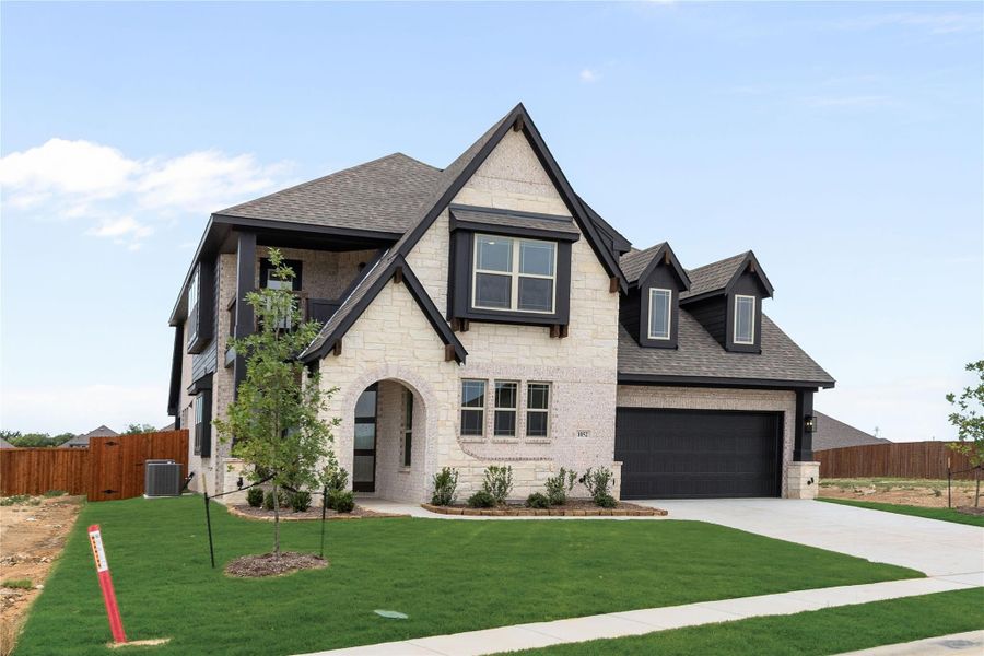 Two-story home with cream stone exterior, dark trim, arched entry, and two-car garage with green lawn Two-story home with cream stone exterior, dark trim, arched entry, and two-car garage with green lawn