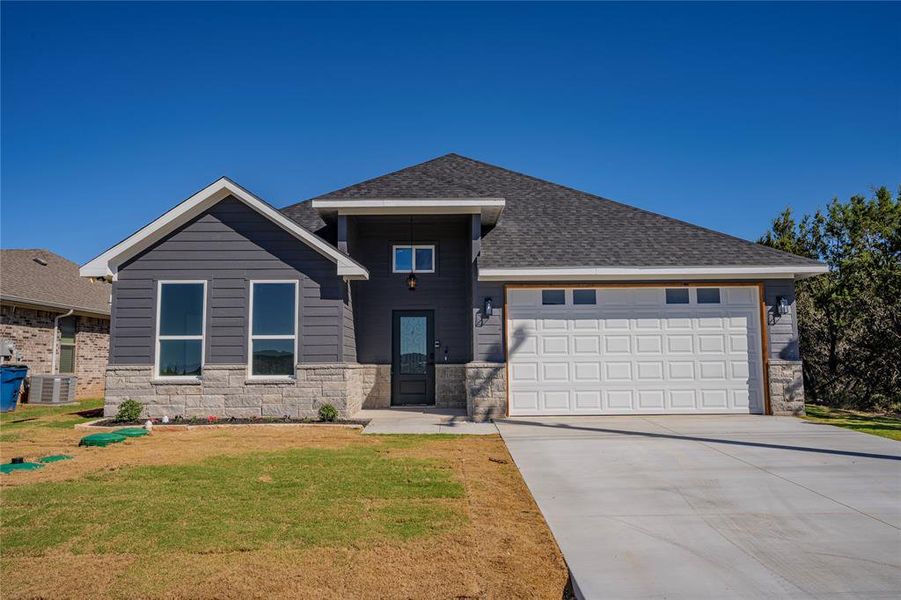 View of front of house featuring a garage, cooling unit, and a front lawn