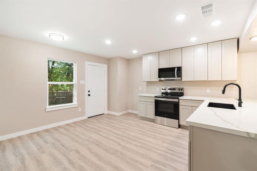 Kitchen with stainless steel appliances, light wood-style flooring, recessed lighting, and light stone countertops