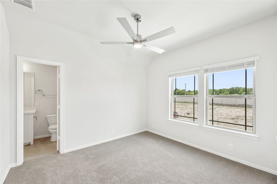 Bedroom with carpet, ceiling fan, two windows, and ensuite bathroom visible through open door Bedroom with carpet, ceiling fan, two windows, and ensuite bathroom visible through open door