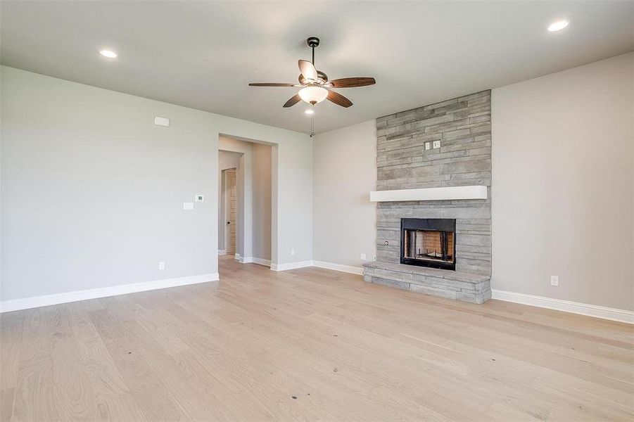 Unfurnished living room with ceiling fan, a fireplace, and light hardwood / wood-style floors