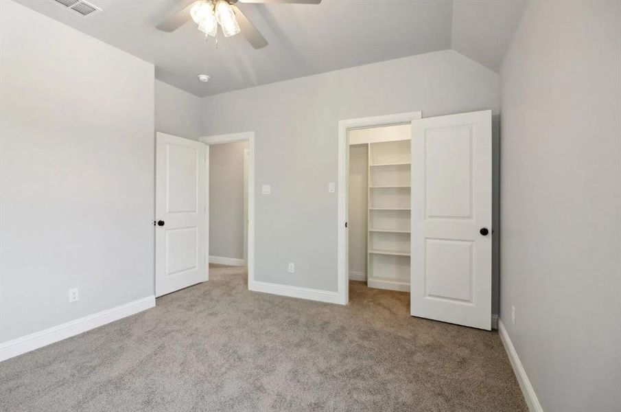 Unfurnished bedroom with ceiling fan, vaulted ceiling, light carpet, a walk in closet, and a closet