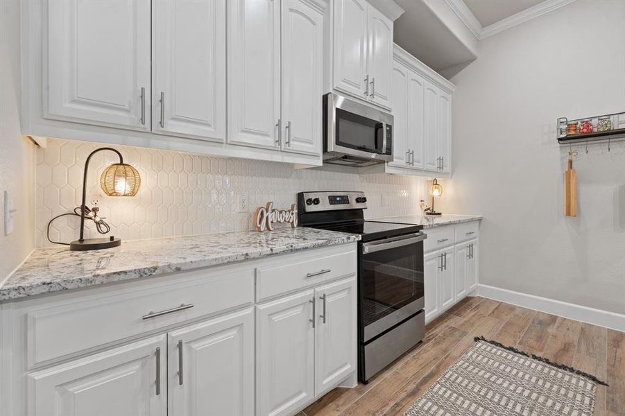 Kitchen with appliances with stainless steel finishes, white cabinets, light stone countertops, tasteful backsplash, and light wood finished floors