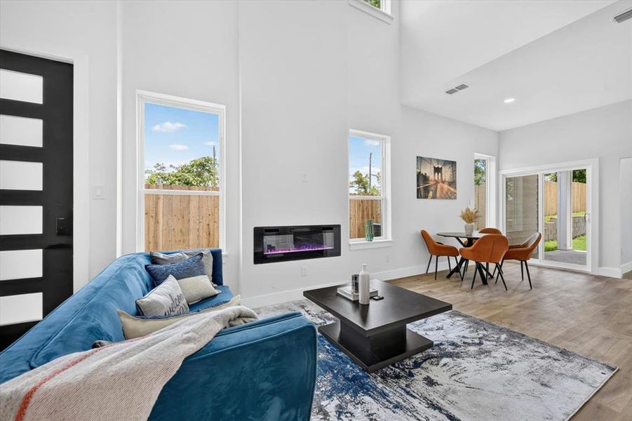 Open-concept living area with high ceilings, an integrated electric fireplace, wood-finish flooring, and a sliding glass door leading to the exterior