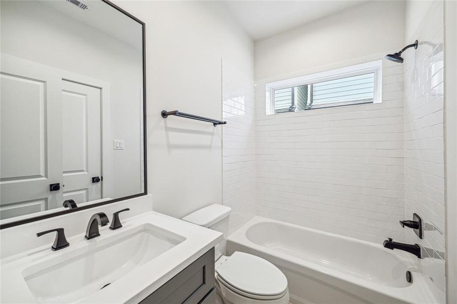 This bathroom features a clean, modern design with a white subway tile shower, a sleek vanity with a large mirror, and contemporary black fixtures. Natural light is provided by a window above the bathtub.