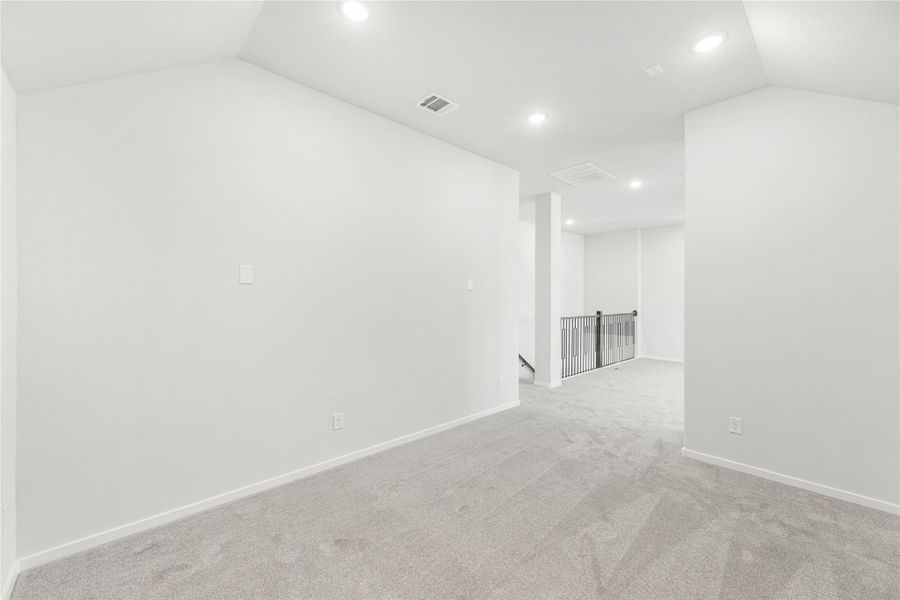 Empty upstairs loft or bonus room with carpet, white walls, recessed lighting, and metal stair railing visible in hallway Empty upstairs loft or bonus room with carpet, white walls, recessed lighting, and metal stair railing visible in hallway