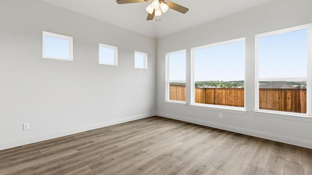 Spacious room featuring wood-finish flooring, multiple windows providing ample ambient light, a ceiling fan with integrated lighting, and white baseboards