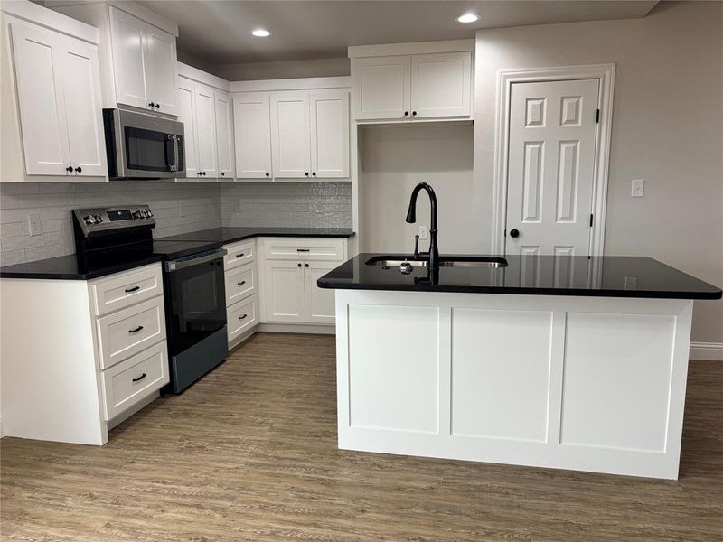 Kitchen featuring electric range, dark wood-style flooring, backsplash, an island with sink, and stainless steel microwave